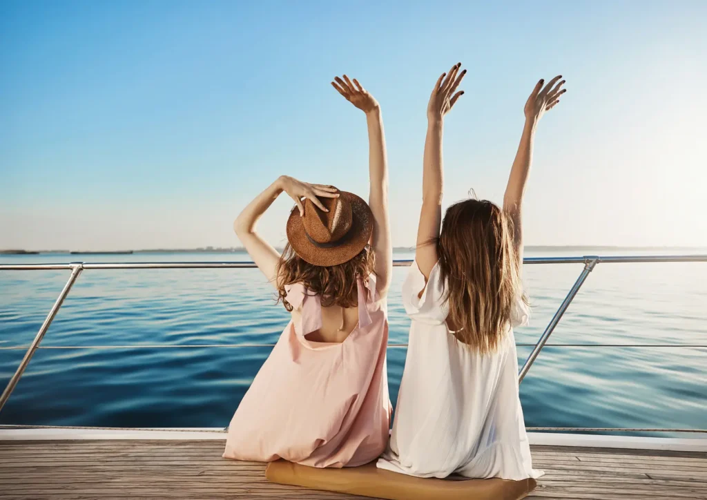 outdoor back view two young female luxury vacation waving seaside while sitting yacht A
